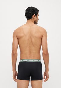 Black boxer briefs with a green logo waistband. The fabric appears smooth and stretchy. The view shows the back and side profile details.