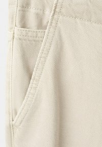 Gros plan sur un tissu beige montrant des coutures détaillées et les coutures de poche d'un pantalon ou d'un jean.
