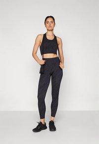 Fekete sportos outfit, amelybe egy testhezálló, rövidített ujjú felső és magas derekú, texturált mintázatú leggings tartozik. Fekete tornacipővel kiegészítve.