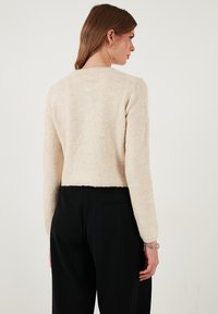 Maglione cropped cremoso e soffice con maniche lunghe e scollo rotondo, abbinato a pantaloni neri; presenta un tessuto texturizzato e un taglio dritto.