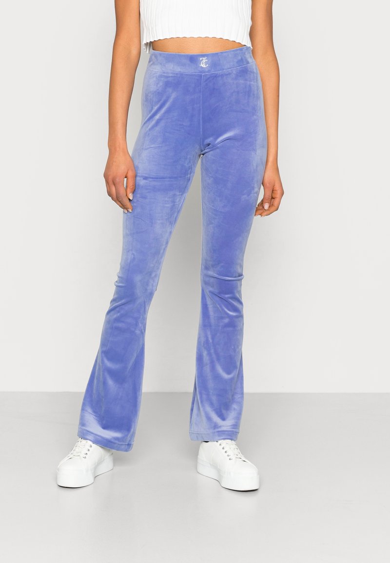 Femme portant un pantalon évasé en velours lavande taille haute, associé à des baskets blanches à plateforme et un top court en maille côtelée blanche.