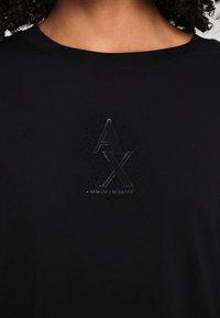 Black cotton T-shirt featuring a glossy black "AX" logo and dotted texture at the center. Crew neck design with smooth, soft fabric.