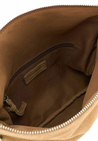 Interno di una borsa in suede marrone con una tasca con cerniera, rivestimento in tessuto liscio e un'etichetta in pelle attaccata. I bordi presentano un sottile dettaglio di cucitura.