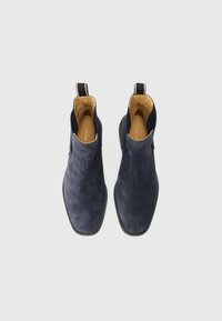 Bottines en daim navy avec une texture lisse, des panneaux latéraux élastiques et une languette de traction ; intérieur doublé en cuir beige ; semelle en caoutchouc plate.