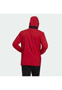 Chaqueta impermeable roja con capucha, con detalles negros en el cuello. Textura suave, mangas largas y un corte relajado.