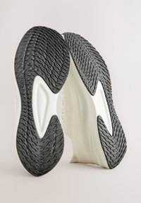 Sportschoenen met een witte en zwarte rubberen buitenzool, getextureerd voor grip. Het bovenwerk heeft een lichtgewicht, ademende meshconstructie.