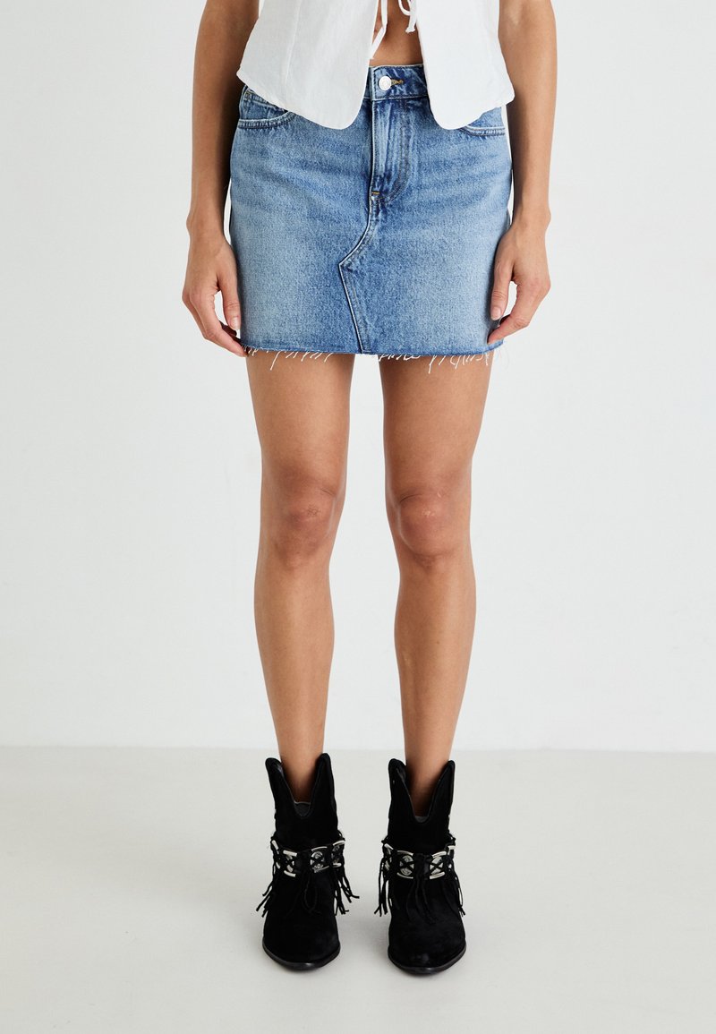 Denim mini krilo v svetlo modri barvi z raztrganim robom, petimi žepi in sprednjim gumbom za zapiranje. V kombinaciji z črnimi semisuvnimi gležnjarji.