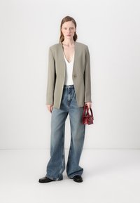 Lys grå single-button blazer brukt over en hvit topp, sammen med vide, blå dongeribukser. Holder en liten rød håndveske. Svarte sko.