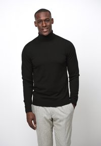 Suéter negro de cuello alto hecho de un material de punto, combinado con pantalones de textura ligera en gris claro. Diseño simple y ajustado.