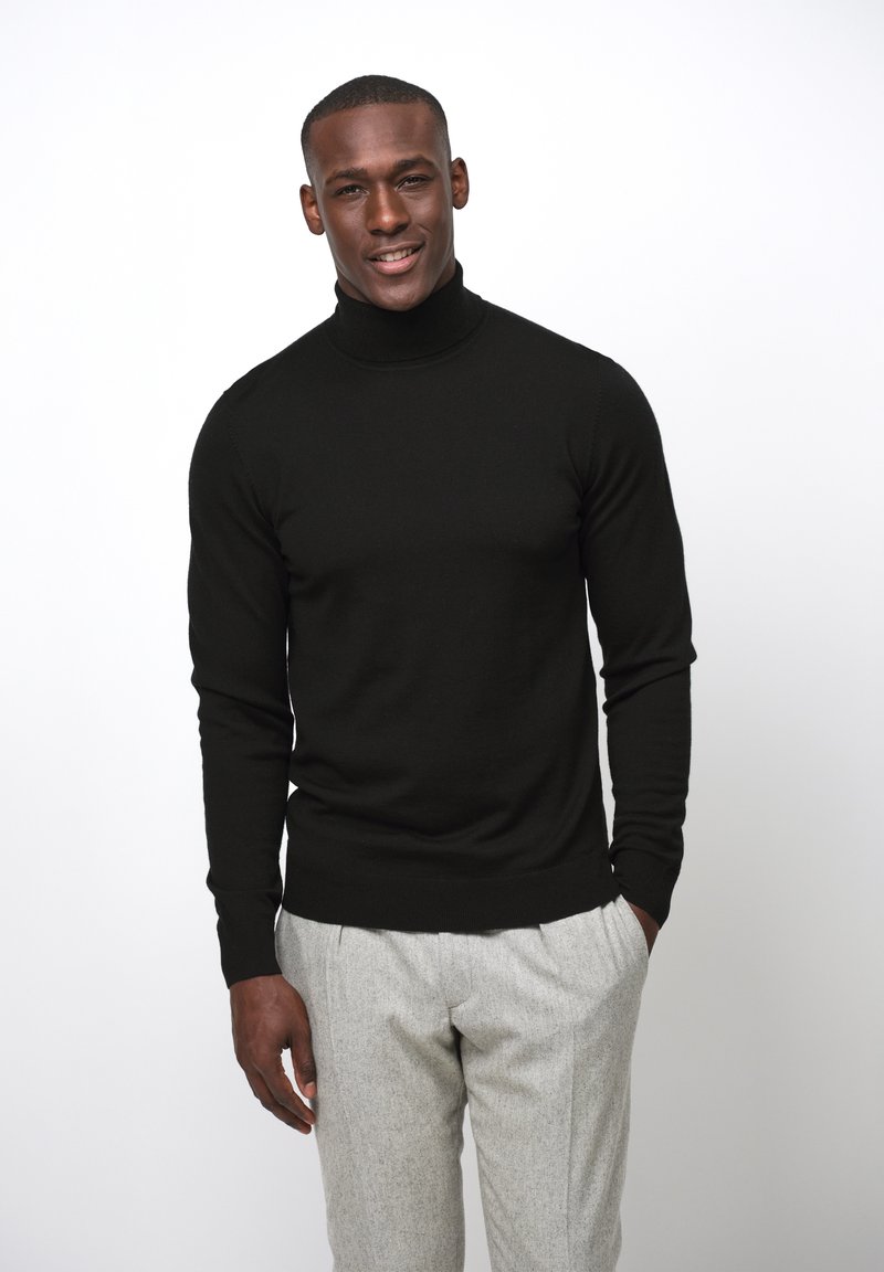 Suéter negro de cuello alto hecho de un material de punto, combinado con pantalones de textura ligera en gris claro. Diseño simple y ajustado.