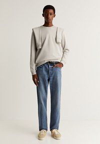 Lichtgrijze sweatshirt met een ronde hals, casual blauwe denim jeans en beige sneakers. Eenvoudig ontwerp met een ontspannen pasvorm.