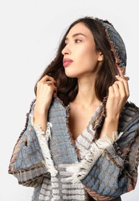 Šarena, teksturirana marama s izgužvanim rubom, koja ima plave, sive i breskvaste pruge. Materijal izgleda tkano, s kapuljačom.