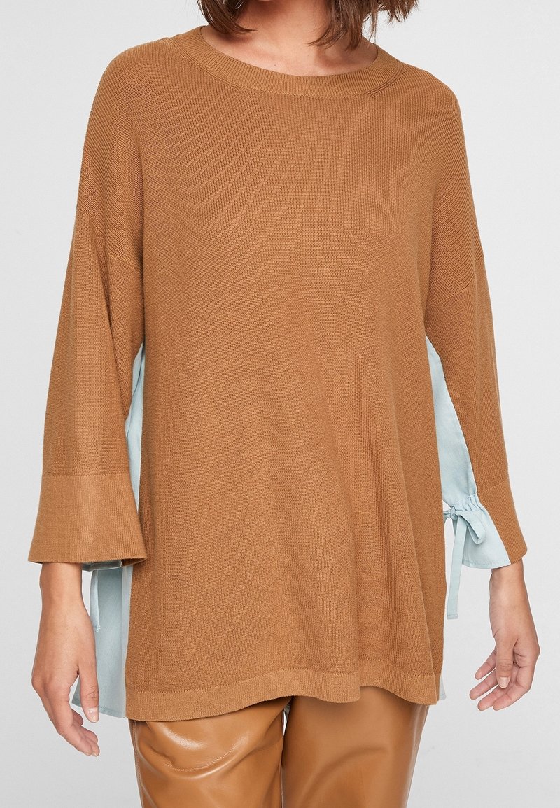 Hnědý pletený svetr s širokými rukávy, s akcentem ze světle modré látky po stranách, jemnou texturou a volným střihem.
