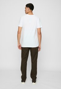 Balta medvilnės t-shirt su apvaliu kaklu, derinama su rudos spalvos kelnėmis. Marškiniai turi trumpas rankoves ir laisvą siluetą; kelnės yra tiesaus žandikaulio su lygiu paviršiumi.