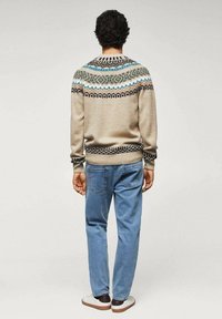 Pull en tricot beige avec un empiècement à motif en vert, bleu et noir. Associé à un jean bleu clair et des chaussures blanches décontractées.