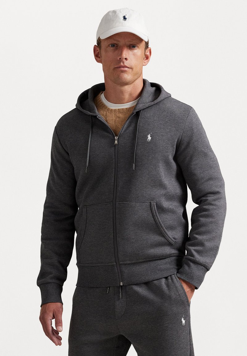 Siva zip-up dukserica od mekog materijala, s prednjim džepovima, kapuljačom s uzicom i malim bijelim polo logom na prsima.