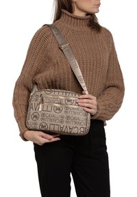 Borsa a tracolla beige con un tessuto testurizzato caratterizzato da un motivo logo ripetuto, hardware in tonalità oro e una tracolla regolabile.