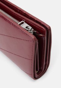 Burgunderfarbenes Lederportemonnaie mit diagonaler Naht, Reißverschluss und glatter Textur. Kompaktes Design mit sichtbaren Kartenfächern im Inneren.