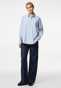 Camicia a righe blu e bianche con bottoni, dal fit rilassato, dotata di taschino sul petto, abbinata a jeans di denim a gamba larga blu scuro.