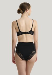 Ensemble comprenant un bralette en dentelle noire et un shorty taille haute, mettant en avant des détails en dentelle florale, un tissu lisse, des bretelles ajustables et des bords à volants.