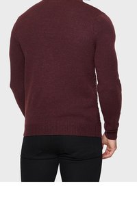 Maglione in maglia bordeaux con texture a coste, design aderente e maniche lunghe. Presenta dettagli laterali e un classico scollo rotondo.