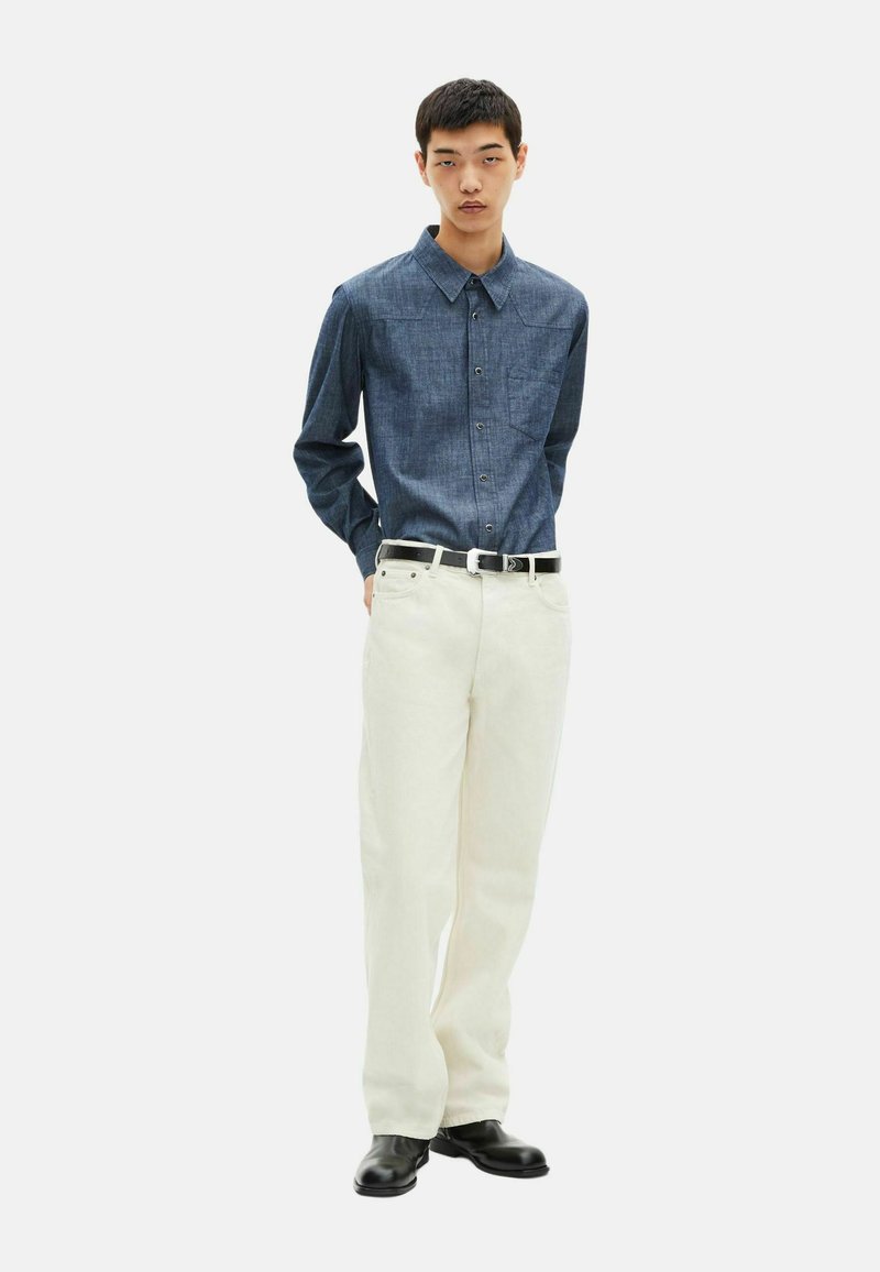 Jeansskjorta med knappar i mörkblått, lång ärm, med en bröstficka. Vita smala byxor, svart bälte och svarta skor fulländar outfiten.