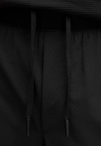 Shorts sportivi neri con texture perforata e lacci piatti. La vita è elastica, offrendo una vestibilità aderente.