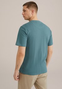 Türkiz színű, rövid ujjú pulóver, texturált bordázott kialakítással. Kerek nyakú, finom oldalsó hasítékkal rendelkezik, világos színű nadrággal párosítva.