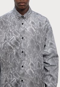 Long-sleeve shirt featuring a gray snake skin pattern, textured fabric, snap collar, and black buttons. Includes printed white text details.