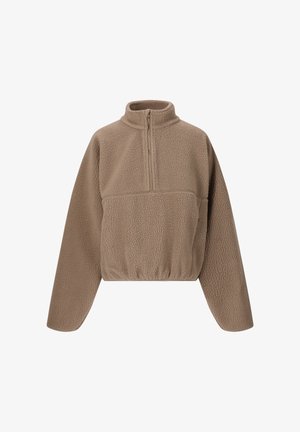 Brun fleecepullover med høj krave, kombineret med sorte leggings med hvid tekst. Lyst grå sneakers med en lys brun sål fuldender looket.