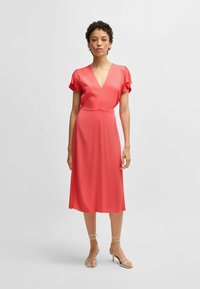 Coral midi dress with short flutter sleeves, V-neckline, and fitted waist. Smooth fabric with a subtle sheen and A-line silhouette.