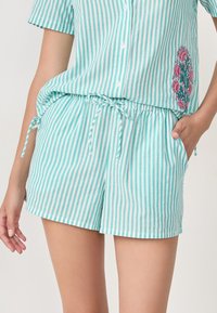 Gestreepte pyjama's in lichtblauw en wit, met een bloemenborduursel aan de zijkant van het shirt. De shorts hebben een elastische tailleband en zijzakken.