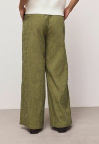 Grün-schwarz kariere, weit geschnittene Hose aus strukturiertem Stoff. Mit hoher Taille und lockerem Sitz, kombiniert mit schwarzen Schuhen.