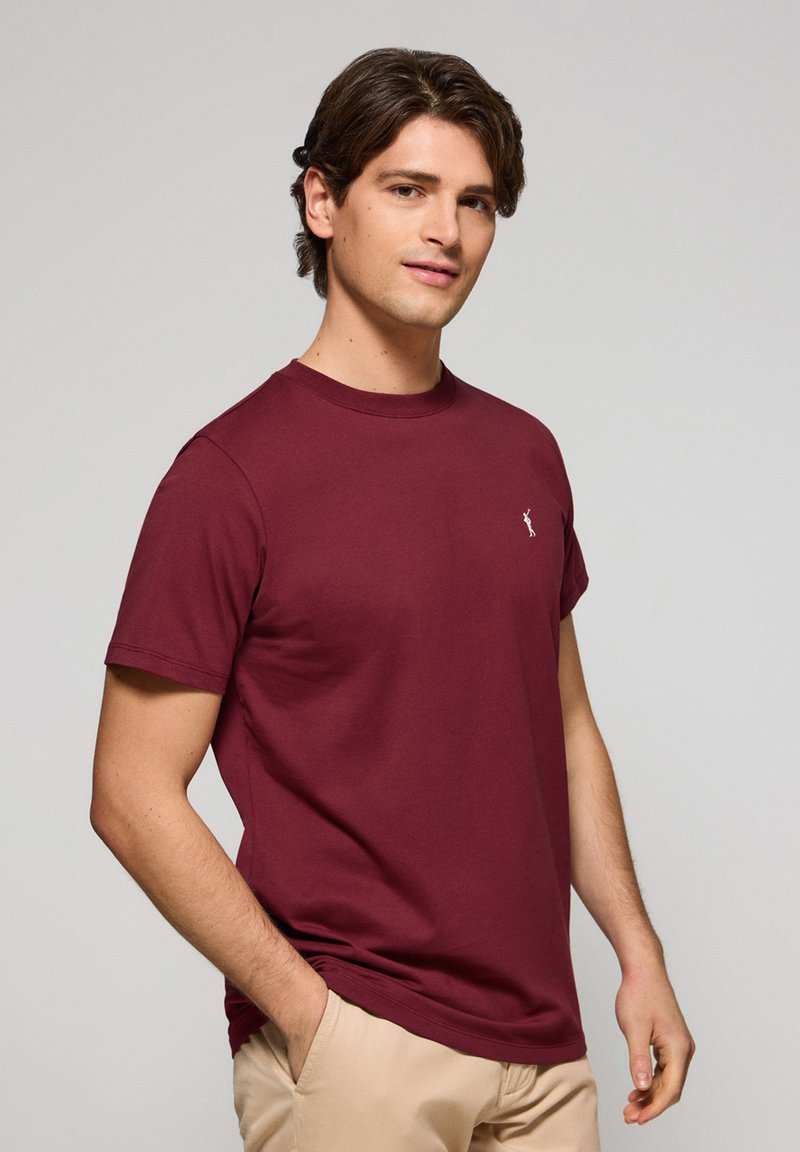 Bordeaux katoenen T-shirt met korte mouwen en een ronde hals; heeft een klein wit logo op de borst. Gladde textuur, casual pasvorm.