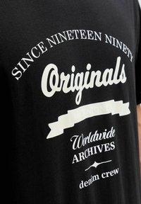 Czarna koszulka z białym napisem "Od dziewiętnastego dziewięćdziesiątego oryginały Jack & Jones Światowe archiwa dżinsowe crew."