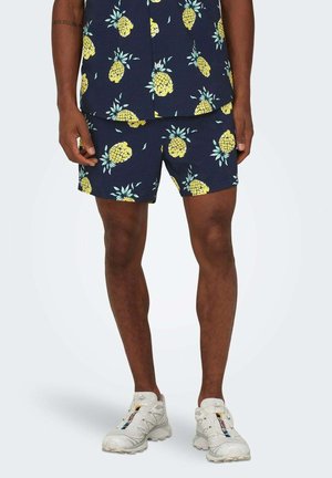Pantalones cortos azul marino y camiseta a juego decorados con piñas amarillas y hojas verdes. Hechos de una tela ligera, adecuada para climas cálidos.
