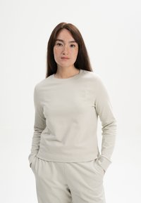 Helles beiges Langarmoberteil aus weichem Stoff, mit rundem Ausschnitt und minimalistischem Design in lockerer Passform.