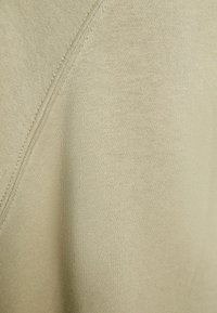 Ljust beige tyg med en slät struktur, som har en subtil diagonal sömsdetalj. Nära bild av stickat vävmönster.