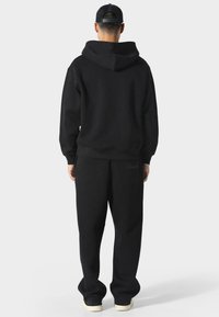 Sudadera negra con capucha y pantalones de chándal a juego, fabricados en un tejido suave. La sudadera presenta una gran capucha y puños acanalados, mientras que los pantalones tienen un corte relajado.