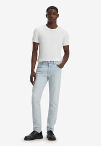 Hellblau denim Jeans mit schmaler Passform, kombiniert mit einem taillierten weißen Rundhals-T-Shirt und schwarzen Schnürschuhen. Sanfte Textur, klassisches Design.