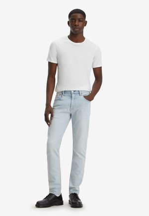 Jeans de mezclilla azul claro con corte slim, combinados con una camiseta de cuello redondo blanca ajustada y zapatos negros con cordones. Textura suave, diseño clásico.