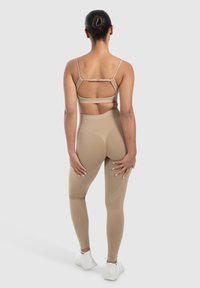 Beige sports-bh med udskæringsdesign, parret med matchende højtaljede leggings med en glat tekstur og subtile konturlinjer.