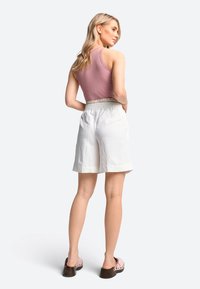 Lichtroze geribde tanktop gecombineerd met witte linnen shorts met een elastische tailleband. Eenvoudig ontwerp, shorts tot halverwege de dijen en bruine klompen.