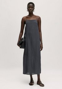 Donkergrijze, mouwloze maxi-jurk met dunne bandjes, gestructureerde stof, een losse pasvorm, gecombineerd met een zwarte clutch en stijlvolle platte sandalen.