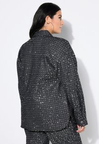 Schwarze, funkelnde Übergröße-Jacke mit texturiertem Finish, ausgestattet mit einem spitzen Kragen und Knopfdetails an den Manschetten. Rückansicht gezeigt.