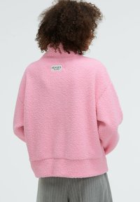 Rosa Fleece-Pullover mit hohem Kragen und lockerer Passform. Verfügt über ein Etikett auf der Rückseite, eine strukturierte Oberfläche und einen gerippten Saum.