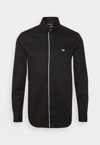 Camicia nera con bottoni, maniche lunghe, patta bianca a contrasto e un piccolo logo sul petto sinistro. Materiale in cotone con una texture liscia.