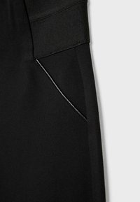 Pantaloni sportivi neri con una ampia vita elasticizzata e una tasca laterale con un elegante profilo nero. Tessuto dalla texture morbida.