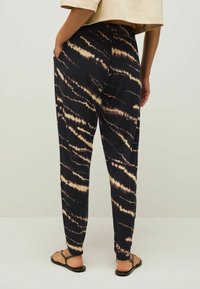 Zwart tie-dye broek met crèmekleurige golvende patronen, voorzien van zijzakken en een relaxed fit. Het materiaal lijkt zacht en lichtgewicht.
