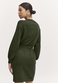 Abito lavorato a maglia verde scuro, con maniche lunghe, vita con cintura e silhouette aderente. Tessuto morbido con polsini e orlo a costine.
